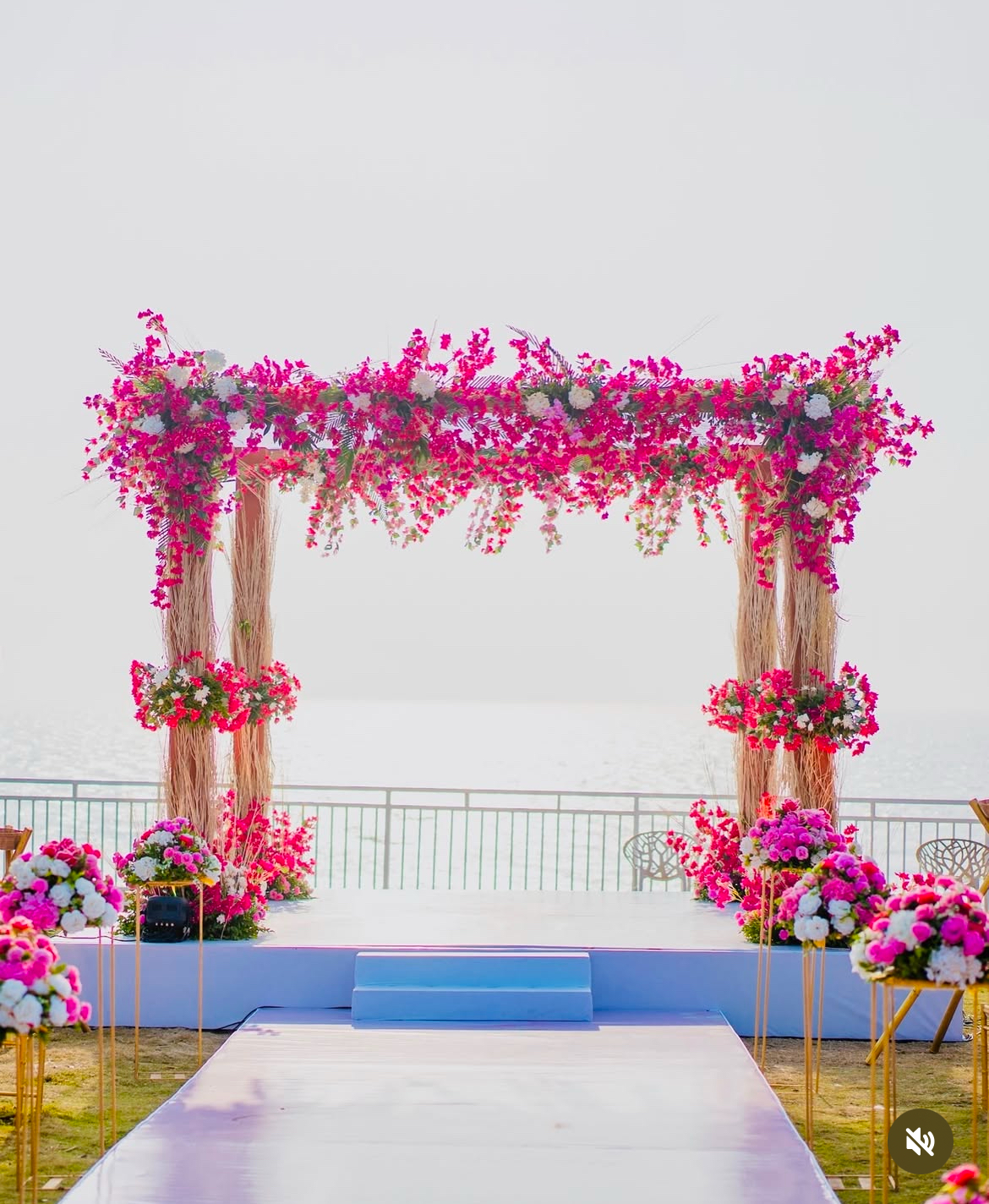 A stunning beachside mandap with white drapes, cherry blossoms, and intricate floral arrangements, set against the backdrop of the turquoise ocean in Goa.